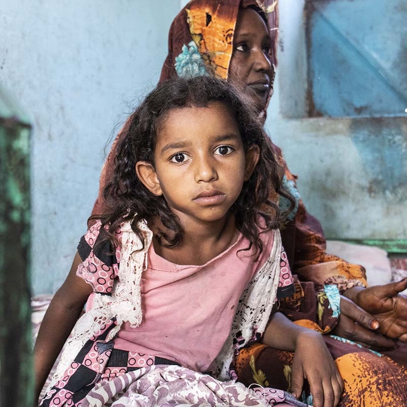 In Sudan, a girl sits with her mother at a health clinic. 