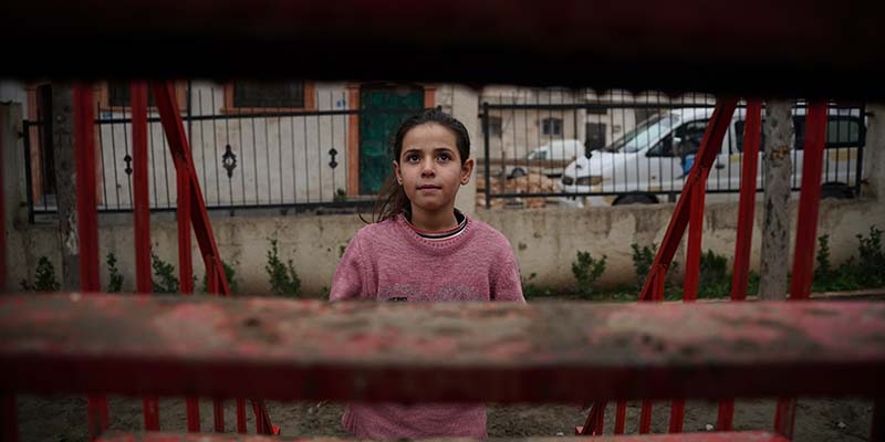In Syria, a girl stands in front of a building that has been destroyed.