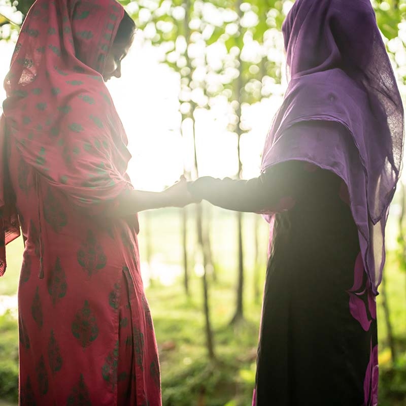 In Bangladesh, two girls laugh and smile while holding hands against the sunrise. 